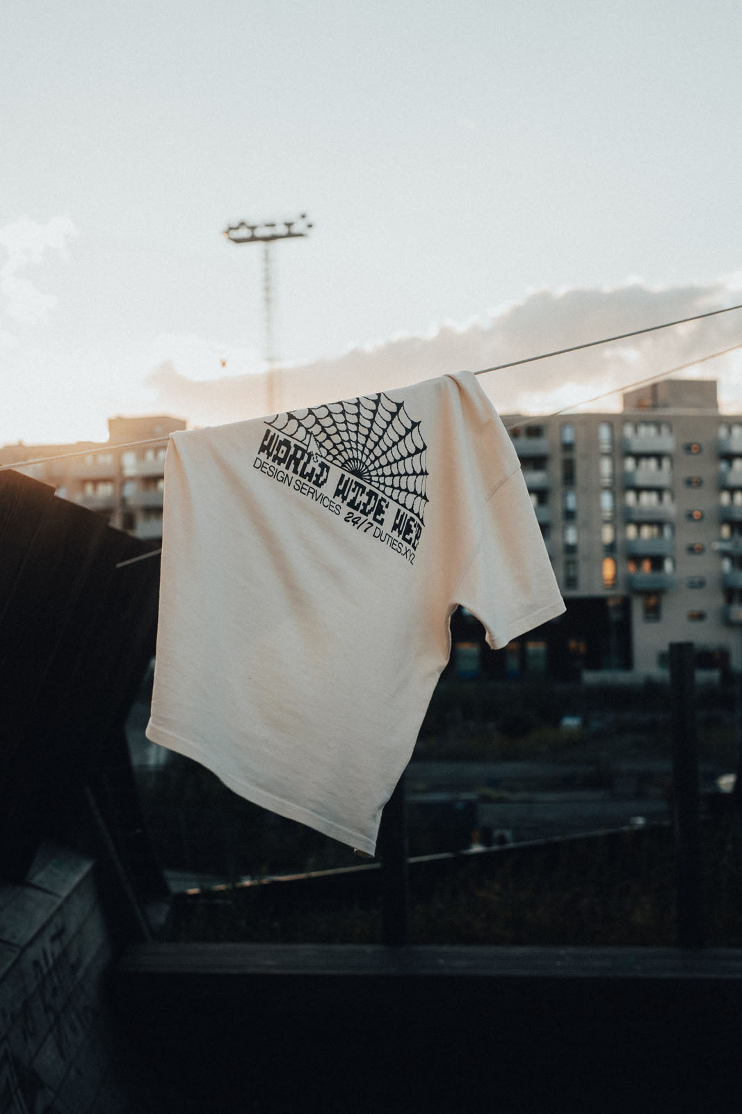 Photo of an Ecru-colored Duties World Wide Web T-Shirt hanging on a wire outside.