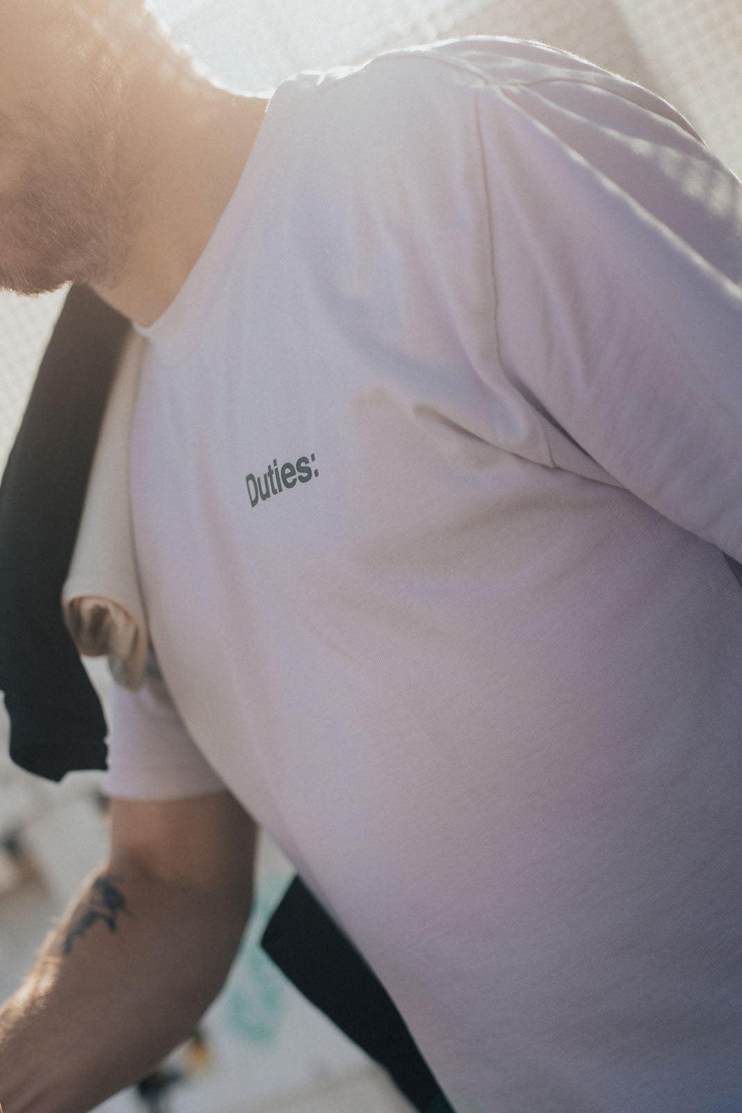 Close-up photo of a man walking outside while wearing an Orchid-colored Duties Code T-Shirt.