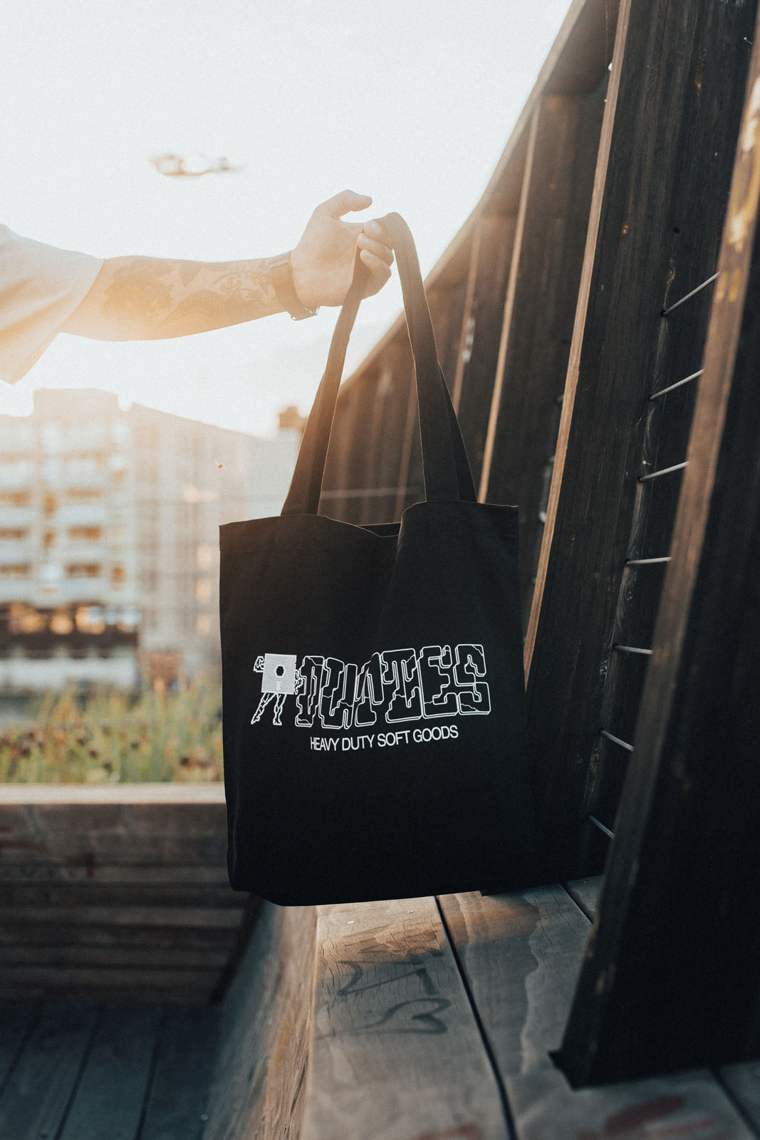 Arm holding up a black Tuff Tote outside, showcasing the white printed graphic on the fabric.