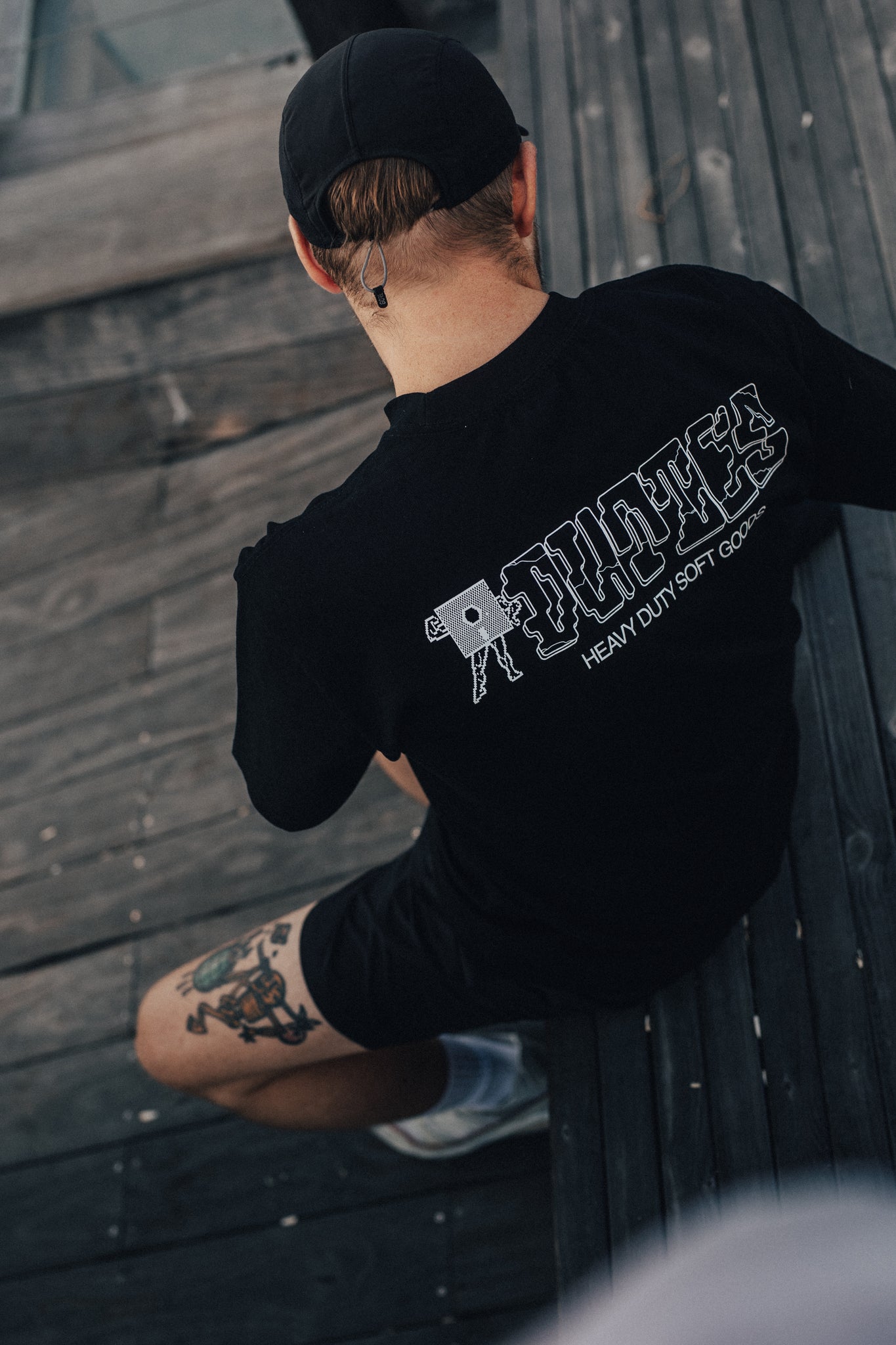 Man sitting outdoors with his back to the camera, showcasing the white Tuff Tee print on the back of a black T-shirt.