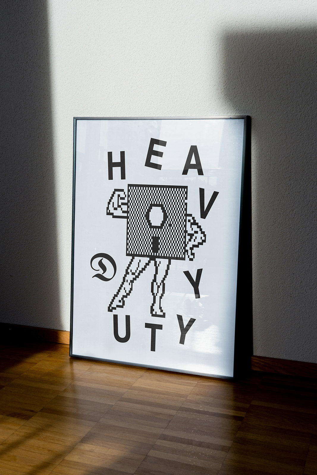 Framed Duties Tuff print poster featuring a pixel illustration of a floppy disc with arms and legs, as well as text saying 'HEAVY DUTY', standing on a white floor and leaning against a white wall.